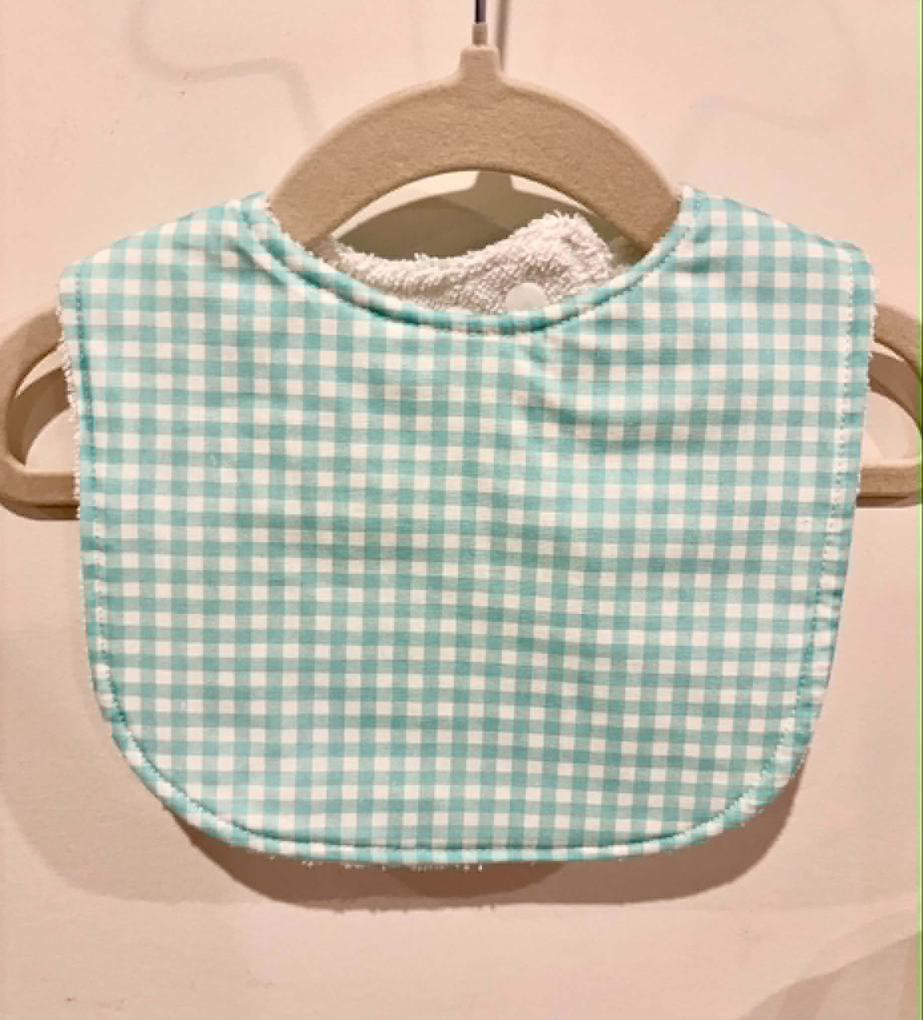 Aqua gingham baby bib hanging on wooden hanger