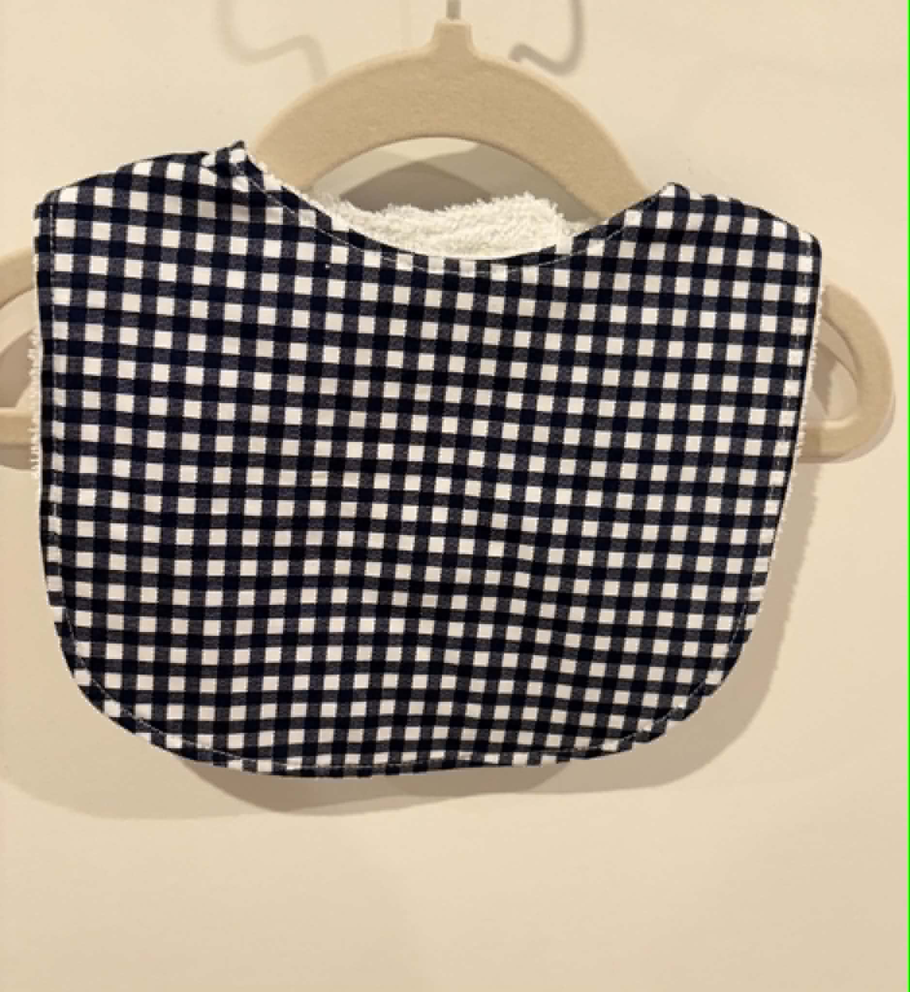 Black gingham baby bib hanging on wooden hanger