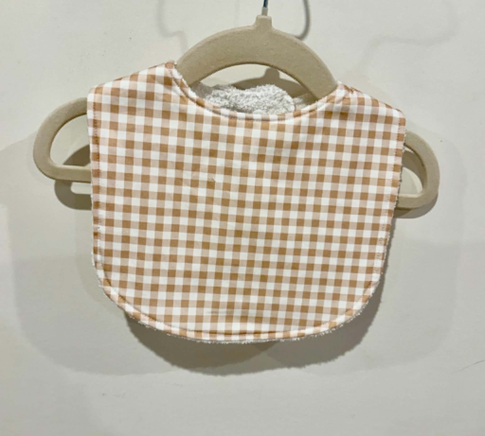 Brown gingham baby bib on wooden hanger