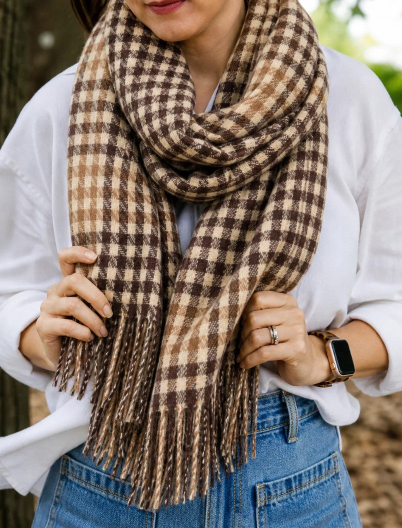 Person wearing a brown and beige plaid scarf with a white shirt and blue jeans.