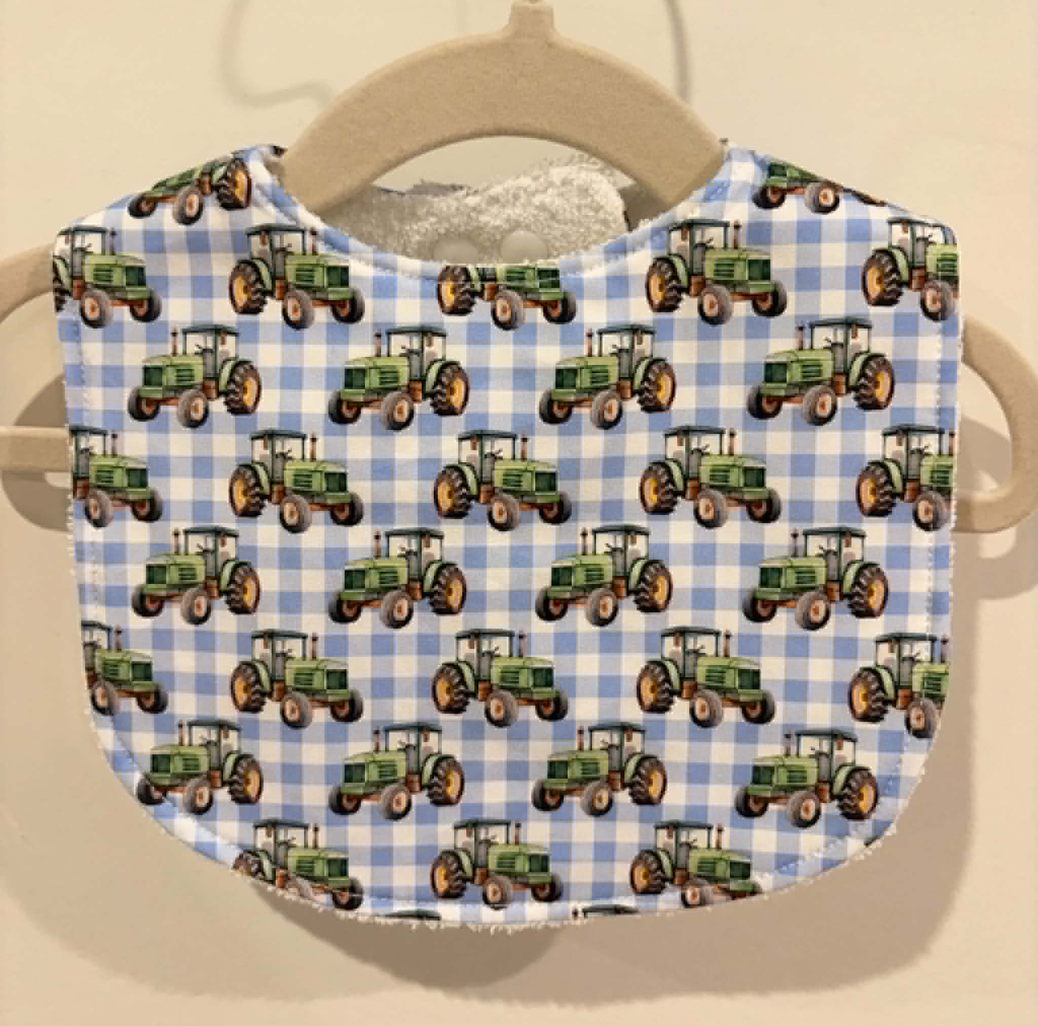 Baby bib with green tractors on blue gingham fabric