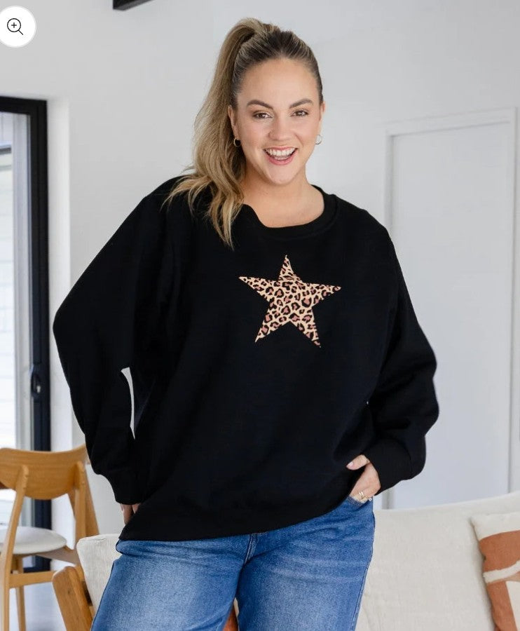 Woman wearing oversized black jumper with leopard print star detail paired with blue jeans.