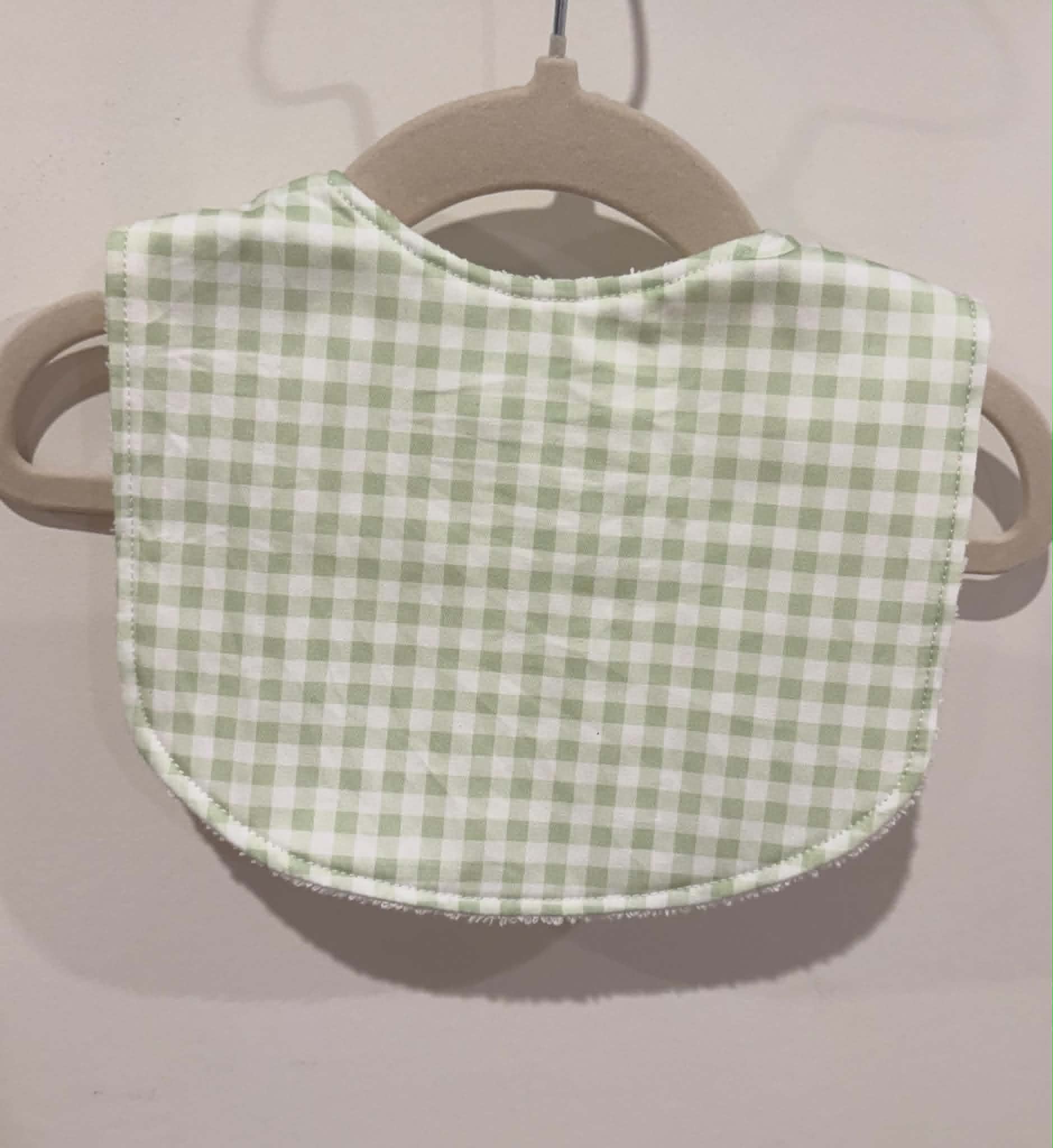 Light green gingham baby bib hanging on wooden hanger