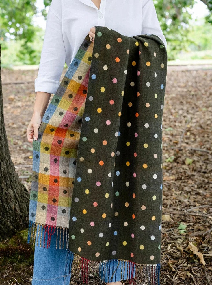 Woman holding reversible olive green scarf featuring polka dots and colourful check pattern outdoors