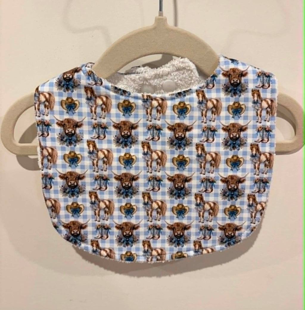 Baby bib featuring ponies and highland cows on blue gingham background