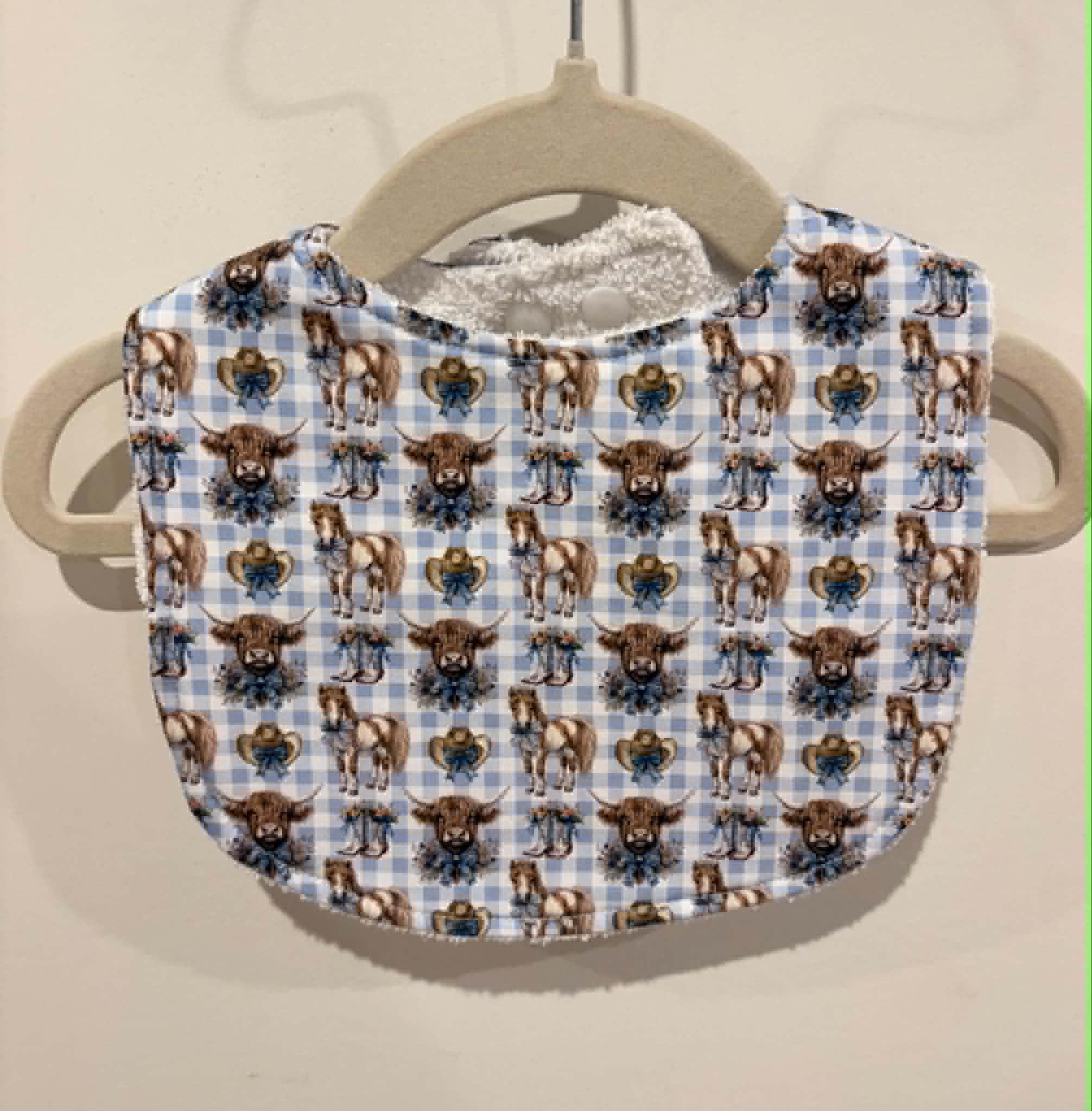 Baby bib featuring ponies and highland cows on blue gingham background