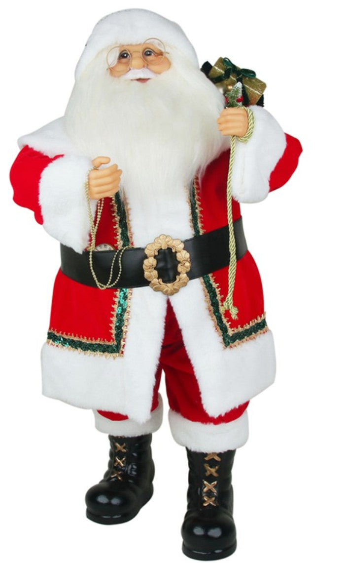 A Santa Claus figurine or decorative statue wearing a red and white suit with a black belt and black boots, holding a green gift bag, on a plain white background.