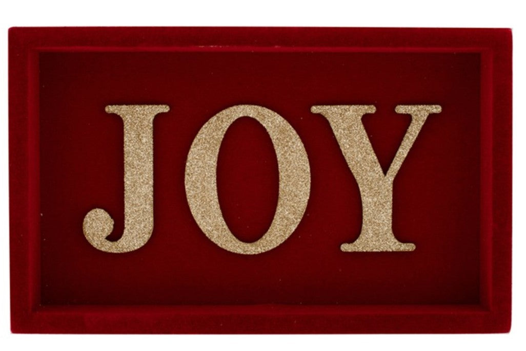 A rectangular red decorative plaque or sign with the word "JOY" in large glittery gold letters, shown against a plain white background.