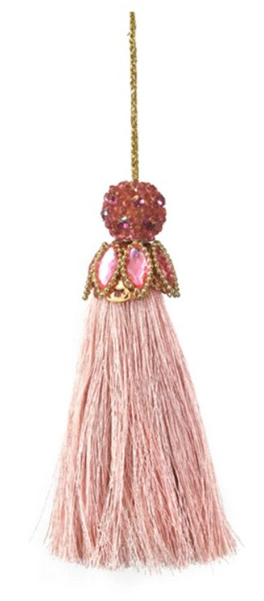 A decorative hanging tassel ornament with a long blush pink fringe, a pink faceted jewel, gold-tone metal detailing, and a gold hanging cord, shown on a plain white background.