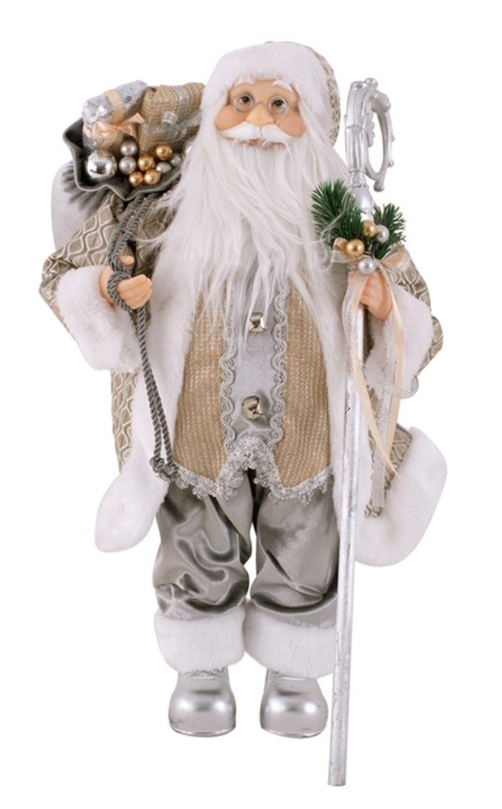 A Santa Claus figurine with a long white beard, wearing a beige and silver patterned coat with white fur trim, carrying a decorated sack on his shoulder and holding a silver staff with green pine branches, isolated on a white background.