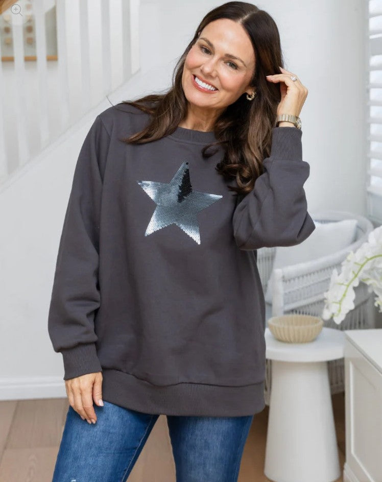 Woman wearing oversized charcoal jumper with silver sequin star detail paired with blue jeans.