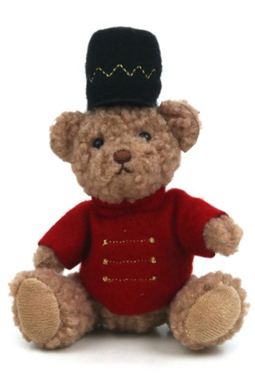 A teddy bear plush toy wearing a red jacket with gold button details and a black top hat with gold zigzag embroidery, set against a plain white background.