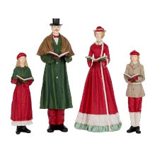 A set of four Christmas-themed figurines depicting a family in historical clothing, including a man in a green coat and top hat, a woman in a red and white gown, a child in a red dress, and a child in a beige military-style coat.