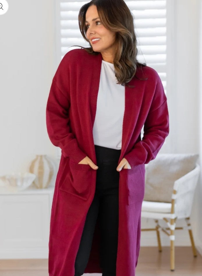 Woman wearing a wine longline knit cardigan with front pockets and relaxed cosy fit styled with black pants and white top