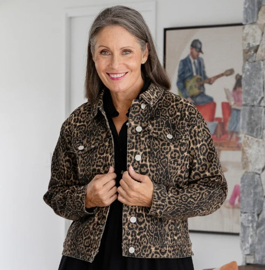 Woman wearing a leopard print jacket indoors with a colorful painting in the background