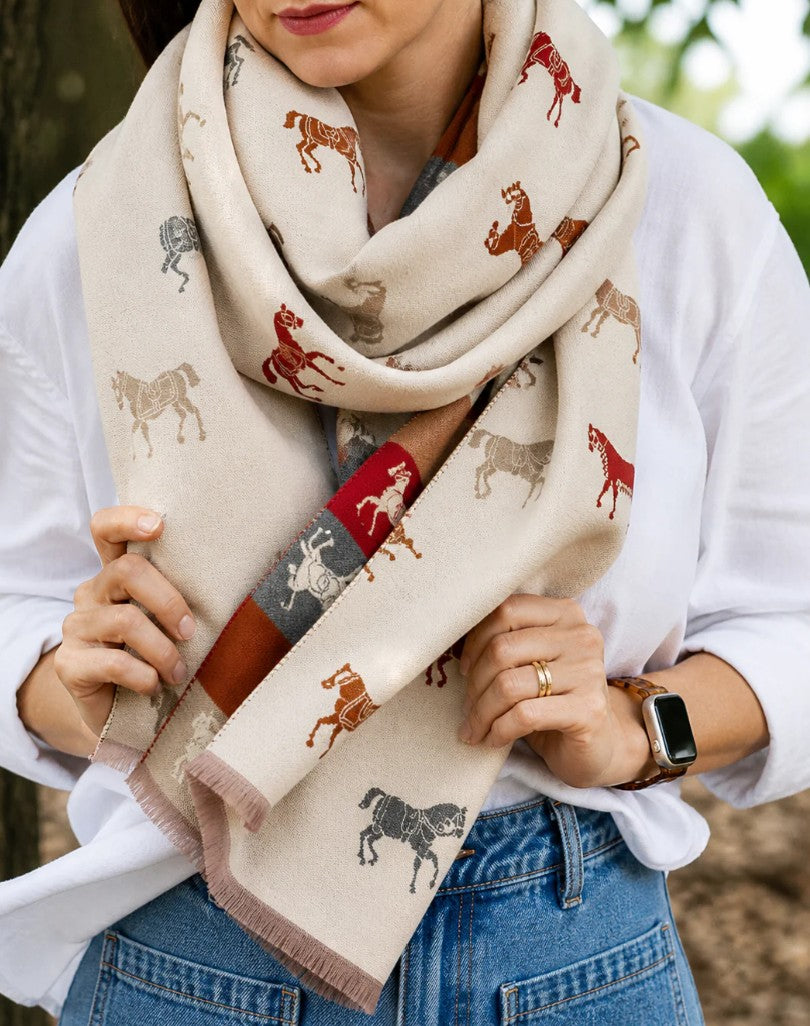 Person wearing a beige scarf with horse patterns, holding it in front of them.